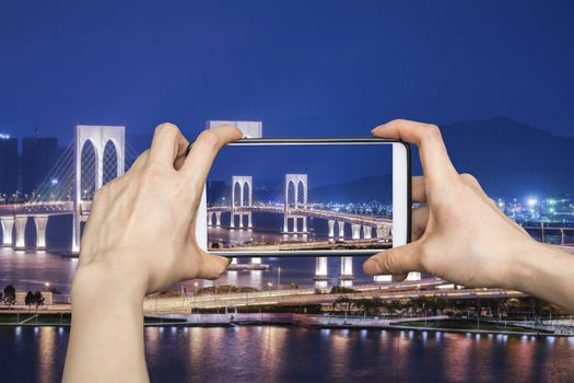 Girl taking pictures on mobile smart phone in View point Bridge in Macau at night