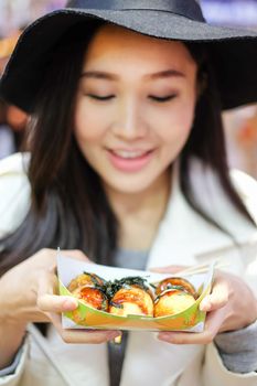 Chinese Asian young female model eating dumpling batter (Takoyaki) on Street in Hong Kong