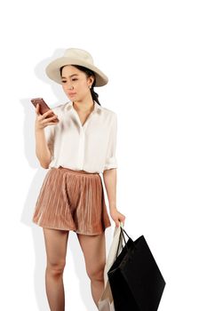 Young asian woman to see a smartphone and hold shopping bag in white background