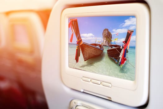 Aircraft monitor in front of passenger seat showing Thai boats and landmark at Po-da island, Krabi Province, Andaman Sea, South of Thailand.