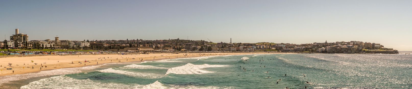 Sydney, Australia - February 11, 2019:  Panorama shot of sandy Bondi beach part and its north shore with housing and nature reserves. Blue water and sky.