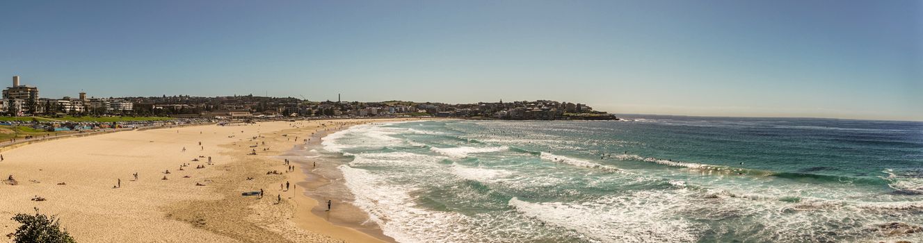 Sydney, Australia - February 11, 2019:  Panorama shot of sandy Bondi beach and its north shore with housing and nature reserves. Blue water and sky.