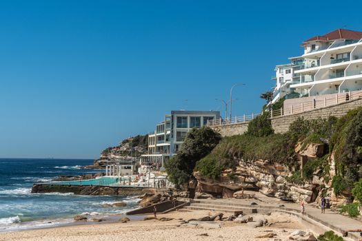 Sydney, Australia - February 11, 2019: Bondi Icebergs Club House and Surf Life Savings with pool, along palth on South shore cliffs. Blue sea and sky. People in photo.