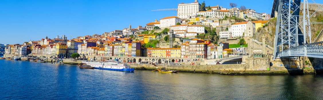PORTO, PORTUGAL - DECEMBER 24, 2017: Panoramic view of the Dom Luis I Bridge, the Douro river and the Ribeira (riverside), with colorful buildings, locals and visitors, in Porto, Portugal
