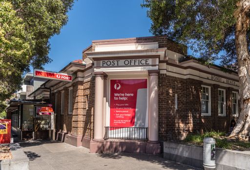 Sydney, Australia - February 11, 2019: Post Office building of Bondi Beach. Street scene with green vegetation. White on red advertisements on columned facade.