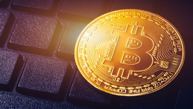 Bitcoin on compuer keyboard in background, symbol of electronic virtual money and mining cryptocurrency concept. Coin crypto currency bitcoin lies on the keyboard. Bitcoin on keyboard.