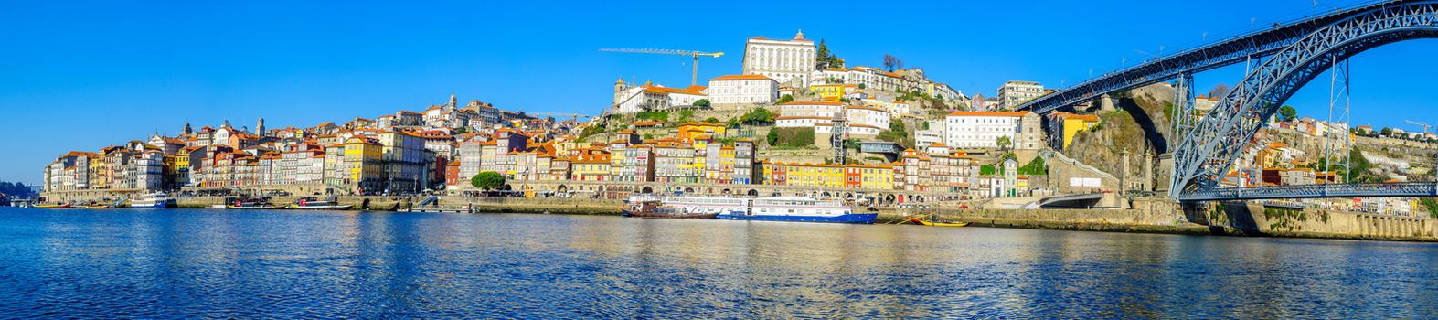 PORTO, PORTUGAL - DECEMBER 24, 2017: Panoramic view of the Dom Luis I Bridge, the Douro river and the Ribeira (riverside), with colorful buildings, locals and visitors, in Porto, Portugal