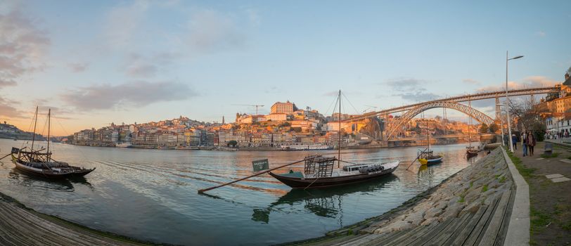 PORTO, PORTUGAL - DECEMBER 24, 2017: Panoramic view at sunset of the Douro river, Dom Luis I Bridge and the Ribeira (riverside), with various boats, locals and visitors, in Porto, Portugal