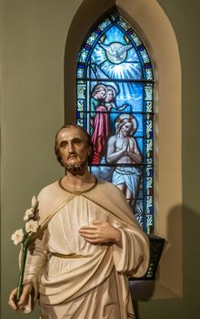 Sydney, Australia - February 12, 2019: Inside Saint Patricks Church on Grosvenor Street opposite of Lang Park. Saint Joseph statue in front of stained glass window showing Jesus Christ and Holy Spirit.