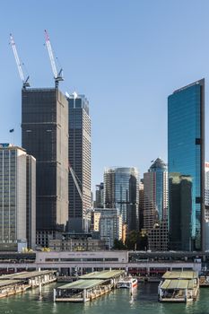 Sydney, Australia - Sydney, Australia - February 12, 2019: Part of ferry terminal and Circular Quay Railway Station plus skyline in back. Highrises under construction with cranes. Evening shot with light blue sky.