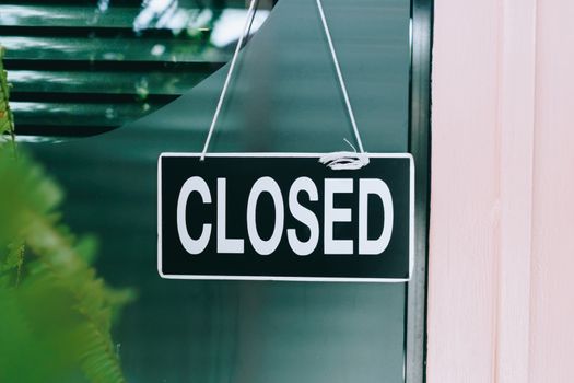 A Sign board of sorry we are closed hang on door of business shop with nature green background