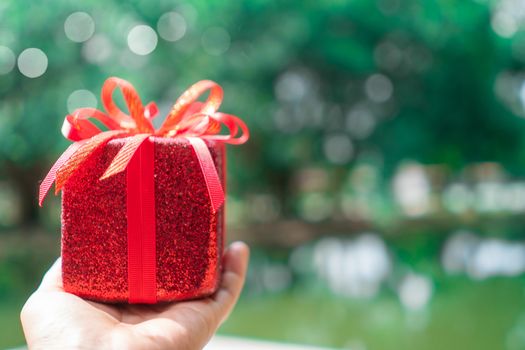 Hand hold gift box to someone on green bokeh nature. Celebration holiday concept.