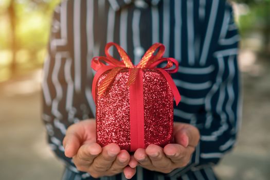 Hand hold gift box to someone on green bokeh nature. Celebration holiday concept.