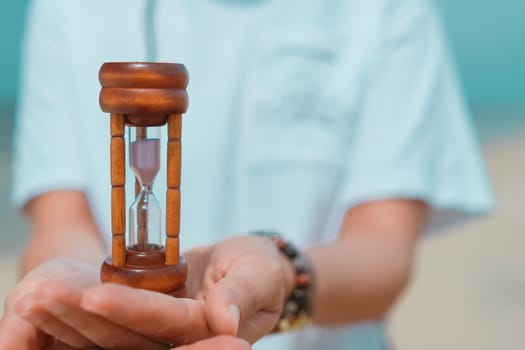 Hand hold small hourglass model show time is flowing on summer beach background.