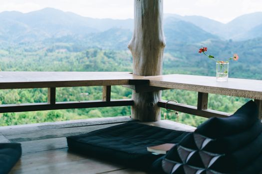Vintage thai style floor seat around with wood table and green nature trees mountain view background. Beautiful terrace of house to relax.