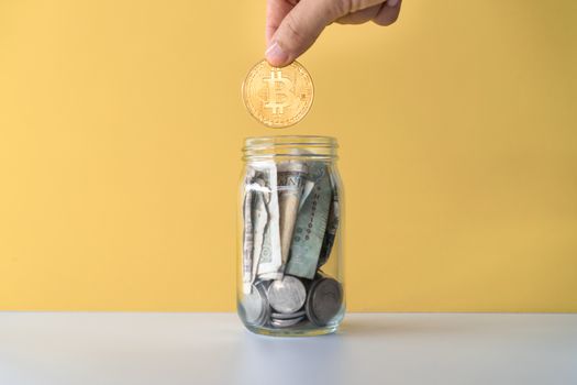 Hand drop gold Bitcoin the jar full of coin and bank notes meaning of saving investment with cryptocurrency digital money fintech online network. Business technology concept.