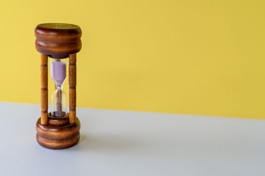 Selective focus of wooden hourglass on yellow background. Time and life concept.