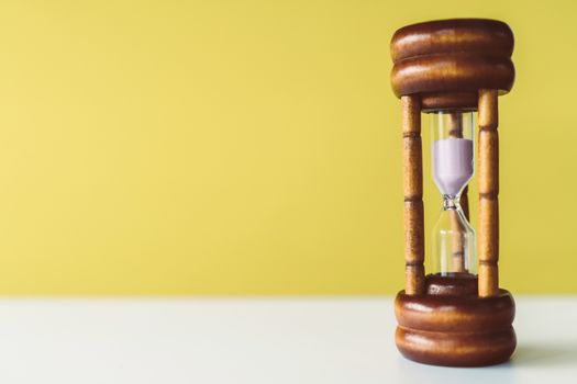 Selective focus of wooden hourglass on yellow background. Time and life concept.