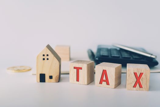 Tax word on wooden cube with objects as gold coin, calculator and mini home model behide white clean background. Business financial loan property concept.