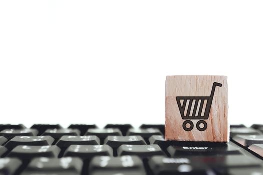 Closed up shopping cart icon on wood cube on computer keyboard. Online shoping business technology concept.