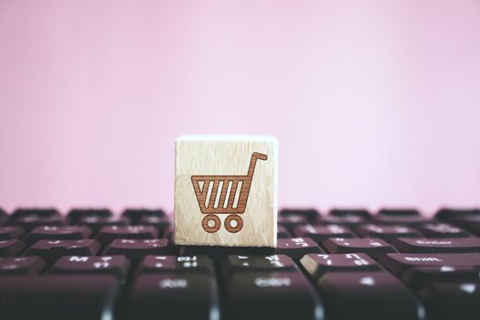 Closed up shopping cart icon on wood cube on computer keyboard. Online shoping business technology concept.