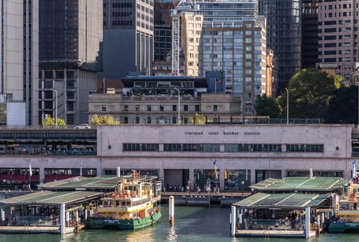 Sydney, Australia - February 12, 2019: Closeup of Ferry terminal and Circular Quay Railway Station. Hightrises in back. Ferries in action. Evening shot with sun falling on boat.