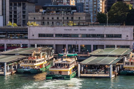 Sydney, Australia - February 12, 2019: Closeup of Ferry terminal and Circular Quay Railway Station. Hightrises in back. Ferries in action. Evening shot with sun falling on boats.