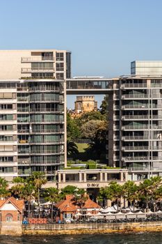 Sydney, Australia - February 12, 2019: Brick stone tower of Government house seen through highrise on eastern shore of Circular bay, Evening sends sunrise right on it. Light blue sky.