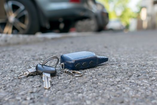 The lost keychain, car alarm remote, lies on the asphalted sidewalk of the road, near an entrance of a house with the parked cars