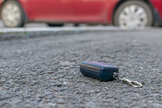 The lost keychain, car alarm remote, lies on the asphalted sidewalk of the road, near an entrance of a house with the parked cars