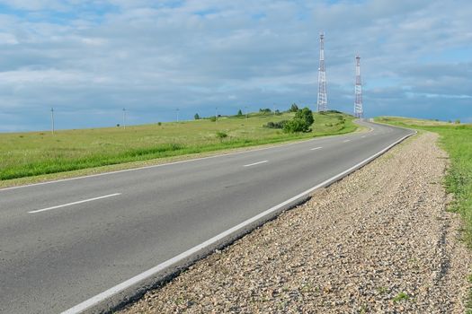 a asphalt country road that runs uphill and has cellular telecommunications towers