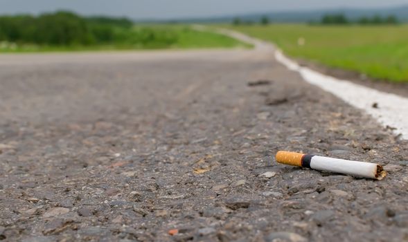 View of cigarette lying on the asphalt on a country road in the cloudy weather