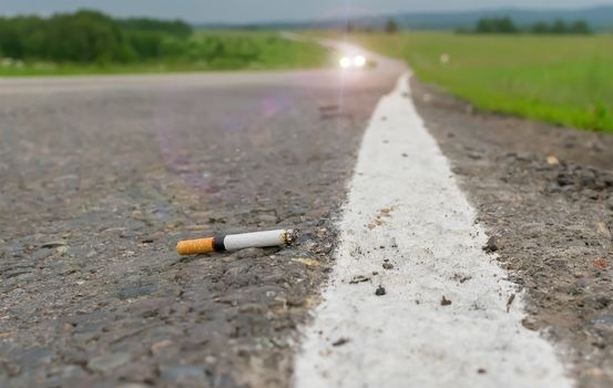 View of cigarette lying on the asphalt on a country road in the cloudy weather in the evening