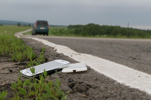 View of a mobile phone lying on the asphalt on a country road in evening time