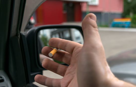 close-up of a cigarette in the hand of a man in the car, who watches the entrance door of the house