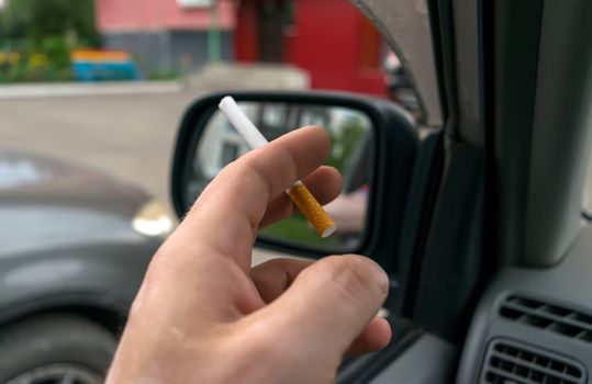 close-up of a cigarette in the hand of a man in the car, who watches the entrance door of the house