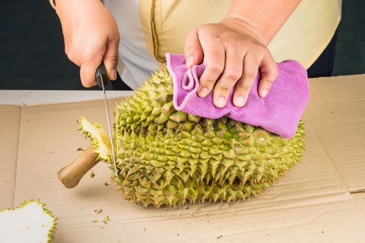 Woman cutting a Durian fruit on the wooden table by using a knife close up. Durian is the one of popular fruit in Thailand.