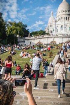 Paris, France - October 6, 2018 - Woman taking a picture of the Basilica of the Sacred Heart among tourists sitting in the grass