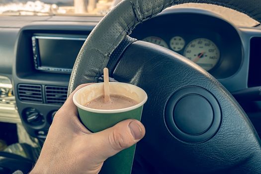 view of a glass of cocoa, chocolate, hot drink in the hand of drivers behind the wheel of a car