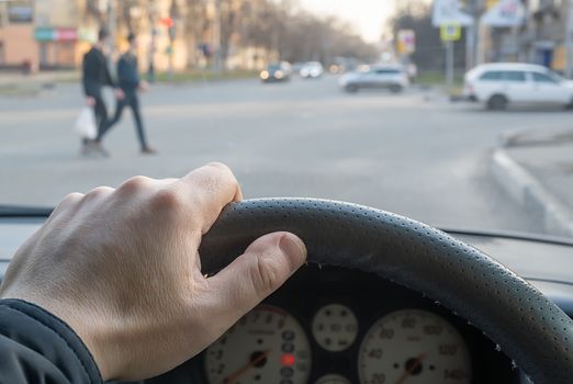 view from the car, the man's hand on the steering wheel of the car, located opposite the pedestrian crossing and pedestrians crossing the road