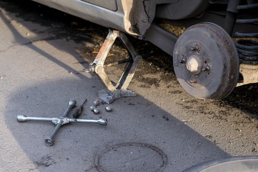 Replacing the rear wheel of the car. The car is mounted on the Jack. On asphalt lie screws, tool and wheel