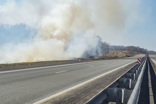 a strong fire, flame and a lot of smoke near the paved highway route, burning dry grass