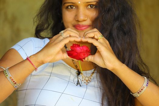 A beautiful woman holds a red rose flower in her heart with fingers, romantic young woman with Two hands making heart sign