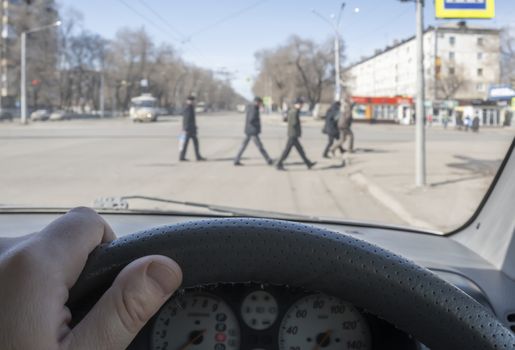 view from the car, the man's hand on the steering wheel of the car, located opposite the pedestrian crossing and pedestrians crossing the road