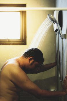 Asian man 40s showering in bathroom for clean a body and relax by bare and water drops from shower to the head and all body