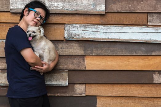 Asian woman and dog happy smile hugging her pat is a dog so cute mixed breed with Shih-Tzu, Pomeranian and Poodle with wooden wall with wood plank background with copy space