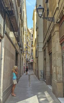 BARCELONA, SPAIN - JULY 6, 2015: Old street in the Gothic Quarter ("Barri gotic") of Barcelona.

Barcelona, Spain - July 6, 2015: Old street in the Gothic Quarter ("Barri gotic") of Barcelona. Woman is standing on the street.