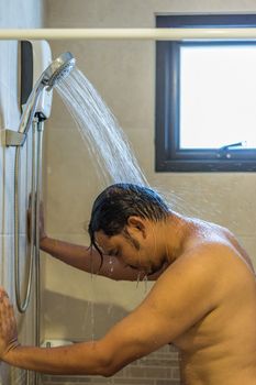 Asian man 40s showering in bathroom for clean a body and relax by bare and water drops from shower to the head and all body