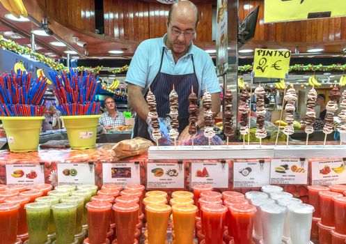 BARCELONA, SPAIN - JULY 6, 2015: Fresh juices assortie at the Boqueria market in Barcelona. It is a large public market in the Ciutat Vella district of Barcelona.

Barcelona, Spain - July 6, 2015: Fresh juices assortie at the Boqueria market in Barcelona. It is a large public market in the Ciutat Vella district of Barcelona. Seller prepares fresh juices.