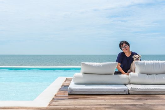 Asian woman and dog happy smile hugging on white beach bed at outdoor swimming pool seaside turquoise sea or ocean with horizon of blue sky at resort or hotel when vacation travel for relax